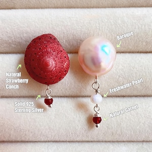 May include: Earrings featuring a natural strawberry conch and a baroque freshwater pearl. The conch earring is a bright red, while the pearl earring is a soft pink. Both earrings have a natural garnet and are made with solid 925 sterling silver.