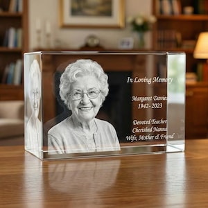 Op de afbeelding: Een helder, rechthoekig kristallen blok met een gegraveerd portret van een oudere vrouw met een bril. De tekst "In Loving Memory" en de naam "Margaret Davies 1942-2023" zijn op de zijkant gegraveerd, samen met "Devoted Teacher, Cherished Nanna, Wife, Mother & Friend."