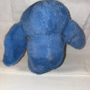 May include: A plush, blue stuffed animal with large, floppy ears. The toy is made of soft, fuzzy material and has a simple, rounded shape. The toy is designed to be cuddled and played with.