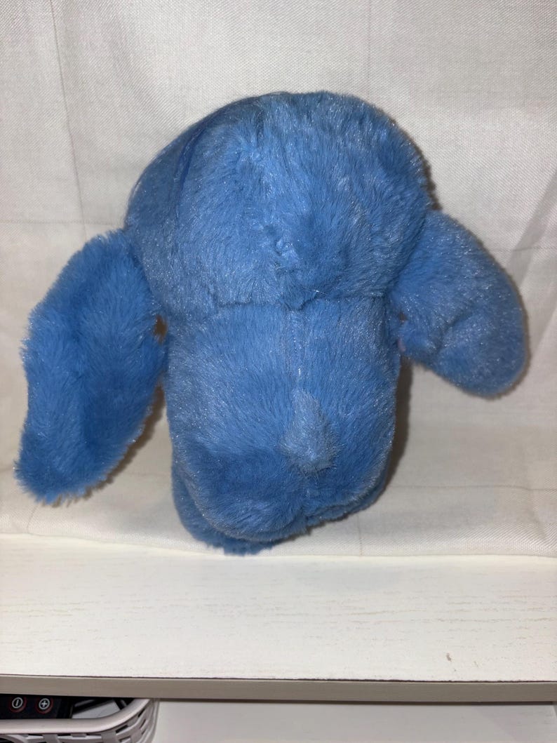 May include: A plush, blue stuffed animal with large, floppy ears. The toy is made of soft, fuzzy material and has a simple, rounded shape. The toy is designed to be cuddled and played with.