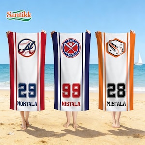 May include: Three beach towels with baseball-themed designs are held up on a sandy beach. Each towel features a different color scheme: red, blue, and orange. Each towel has a number and a name, with baseball-related graphics.