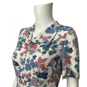 May include: A white dress with a floral print featuring blue, pink and green flowers. The dress has a collared neckline and short sleeves.