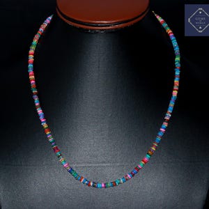 May include: A colorful beaded necklace with a variety of small, round beads in shades of red, blue, green, and yellow. The necklace is displayed on a black surface, showcasing the vibrant colors of the beads. The necklace is approximately 18 inches long.