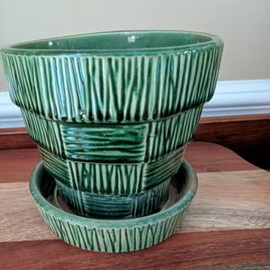 May include: A green ceramic planter with a matching saucer. The planter has a textured, stacked design with vertical and horizontal lines. The planter is approximately 8 inches in diameter and 6 inches tall.