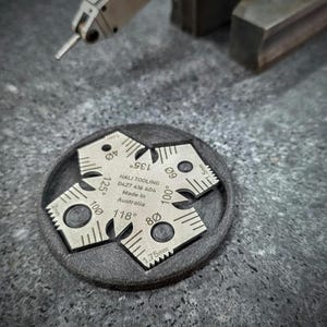 Peut inclure: Gros plan sur des outils de précision en métal. Quatre petites jauges d'angle argentées sont disposées sur une base circulaire grise foncée. Les jauges indiquent des mesures d'angle telles que 40°, 60°, 80°, 100°, 118°, 125° et 135°. Le texte "HALI TOOLING" est visible.