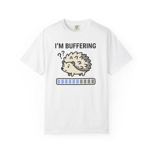 Puede incluir: Camiseta blanca con el texto "I'M BUFFERING" sobre un dibujo animado de un erizo y una barra de carga. El erizo es de color marrón claro con la espalda espinosa gris. La barra de carga es azul y gris.