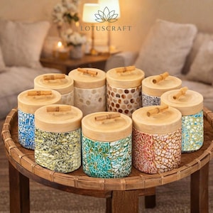 May include: A collection of decorative jars with wooden lids and bamboo handles. The jars have various patterns and colors, including blue, green, yellow, and red. The jars are arranged on a round, woven table. The Lotuscraft logo is visible in the background.