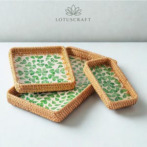 May include: Four woven rattan trays in different sizes. Each tray features a white interior with a green leaf pattern. The trays are square and rectangular, with a natural brown colour. The Lotuscraft logo is visible in the top centre.