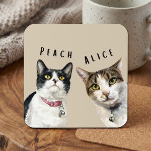 May include: Square coaster featuring illustrations of two cats, one black and white, the other tabby. The names "Peach" and "Alice" are printed above the cat portraits. The coaster is on a wooden surface, next to a mug.