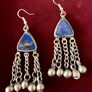 Puede incluir: Un par de pendientes de plata con piedras de lapislázuli azules y cadenas colgantes con cascabeles de plata.