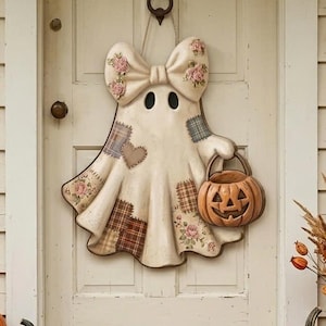 May include: A cream-colored ghost wall hanging featuring a large bow on top, floral and plaid patchwork patterns, and a small orange jack-o'-lantern bucket held in one hand. The ghost is suspended on a light-colored door with a black metal knocker.