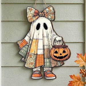 May include: A hanging wall decoration shaped like a ghost wearing a patchwork-style sheet with orange, yellow, and green patterns. The ghost has a large bow on its head, wears orange sneakers, and carries a carved orange jack-o'-lantern bucket.