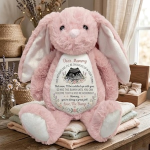 May include: A large, pink plush bunny with long ears and a white belly patch. The patch features text and an ultrasound image. The text reads "Dear Mommy" and a message from "Love, The Bump."
