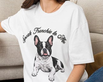 May include: A white short-sleeved t-shirt featuring a graphic illustration of a black and white French Bulldog. Above the dog, the text reads Speak Frenchie to Me in a dark, stylized font. The shirt has a crew neckline and a relaxed fit.