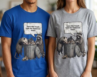 May include: A royal blue t-shirt and a heather gray t-shirt, each featuring a graphic of an opossum and a raccoon standing by a metal trash can. Above the animals is a speech bubble containing the text, Save the Trash Talk for Someone Else!!