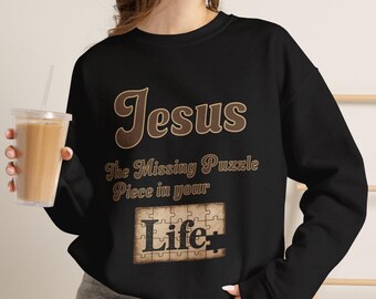 May include: A black long-sleeve sweatshirt featuring the brown text "Jesus The Missing Puzzle Piece in your" above a graphic of a tan jigsaw puzzle piece with the word "Life" printed in black, centered on the front of the garment.