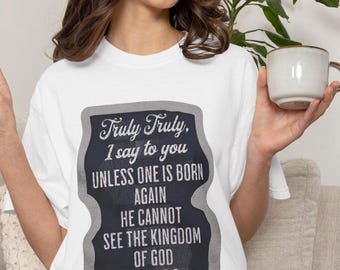 May include: A white short-sleeved t-shirt featuring a dark gray graphic with the text: Truly Truly, I say to you UNLESS ONE IS BORN AGAIN HE CANNOT SEE THE KINGDOM OF GOD JOHN 3:3. The graphic has a distressed texture and a rounded border.