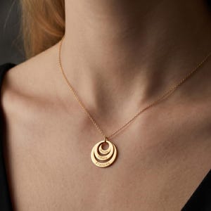 May include: A gold-colored pendant necklace with three connected circular charms. The top charm has a small diamond, and each charm is engraved with a name: "Sammy", "Tiffany", and "Frances". The necklace is worn against a black top.