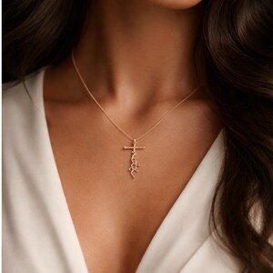 May include: A gold-colored necklace featuring a cross pendant with the word "faith" written in a cursive script. The necklace is worn against a white top, creating a contrast with the skin tone.