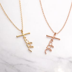 May include: Two necklaces with the word "faith" in a cursive script, attached to a cross pendant. One necklace is gold-colored, and the other is rose gold. Both necklaces are on a delicate chain.