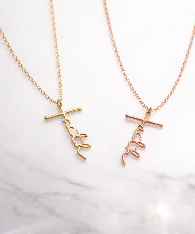 May include: Two necklaces with the word "faith" in a cursive script, attached to a cross pendant. One necklace is gold-colored, and the other is rose gold. Both necklaces are on a delicate chain.