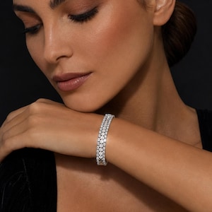 May include: A silver-toned link bracelet featuring three parallel rows of small, clear, sparkling stones. The bracelet has a structured, rectangular link design with a polished metallic finish that reflects light across its surface.