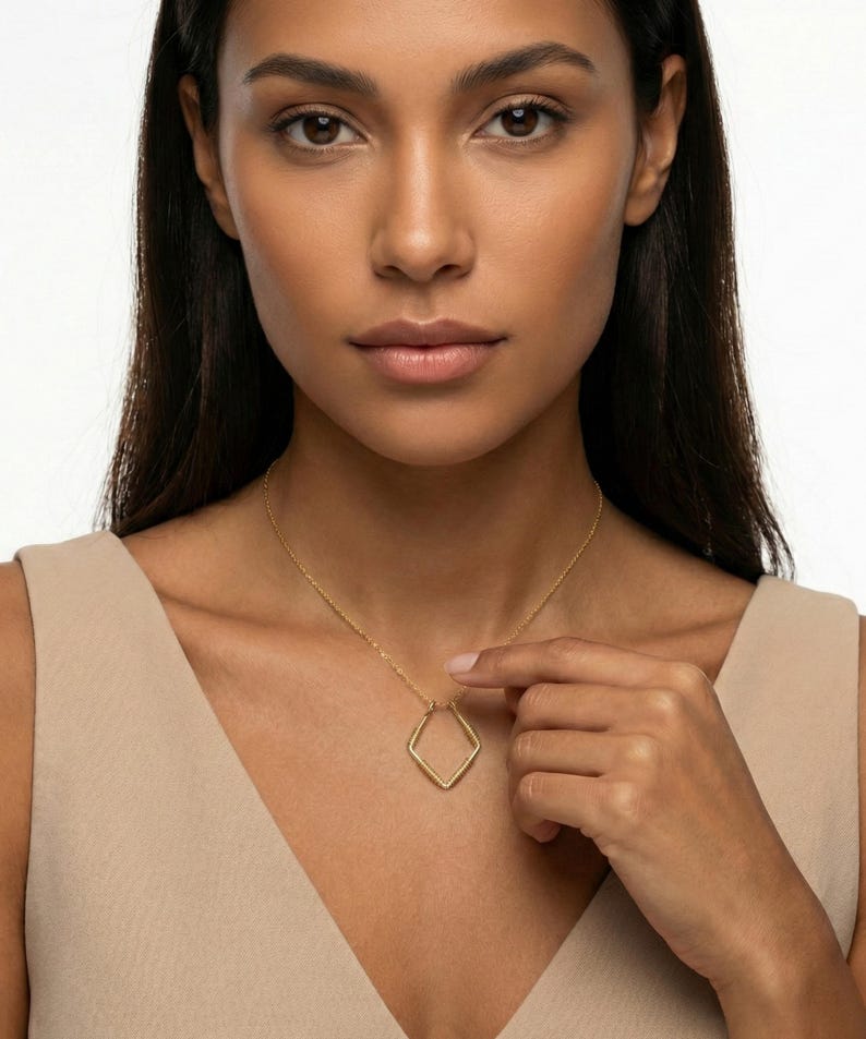 May include: A gold-colored necklace featuring a diamond-shaped pendant. The pendant is suspended from a delicate chain. The woman in the image is wearing a beige top.
