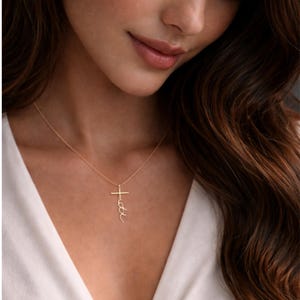 May include: Gold-colored necklace with a cross pendant. The cross features the word "faith" in a delicate script. The necklace is worn against a white top.