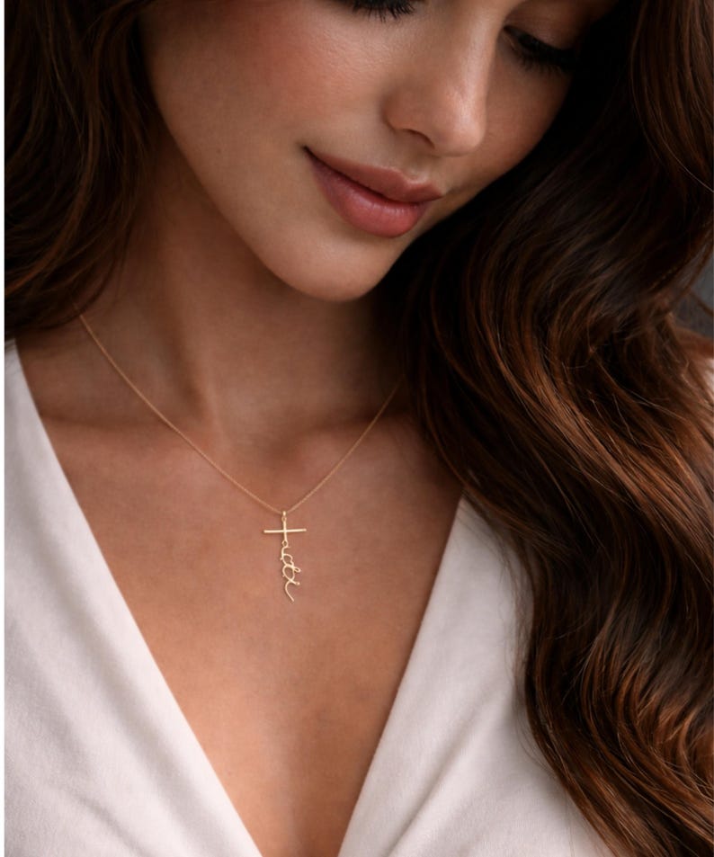 May include: Gold-colored necklace with a cross pendant. The cross features the word "faith" in a delicate script. The necklace is worn against a white top.