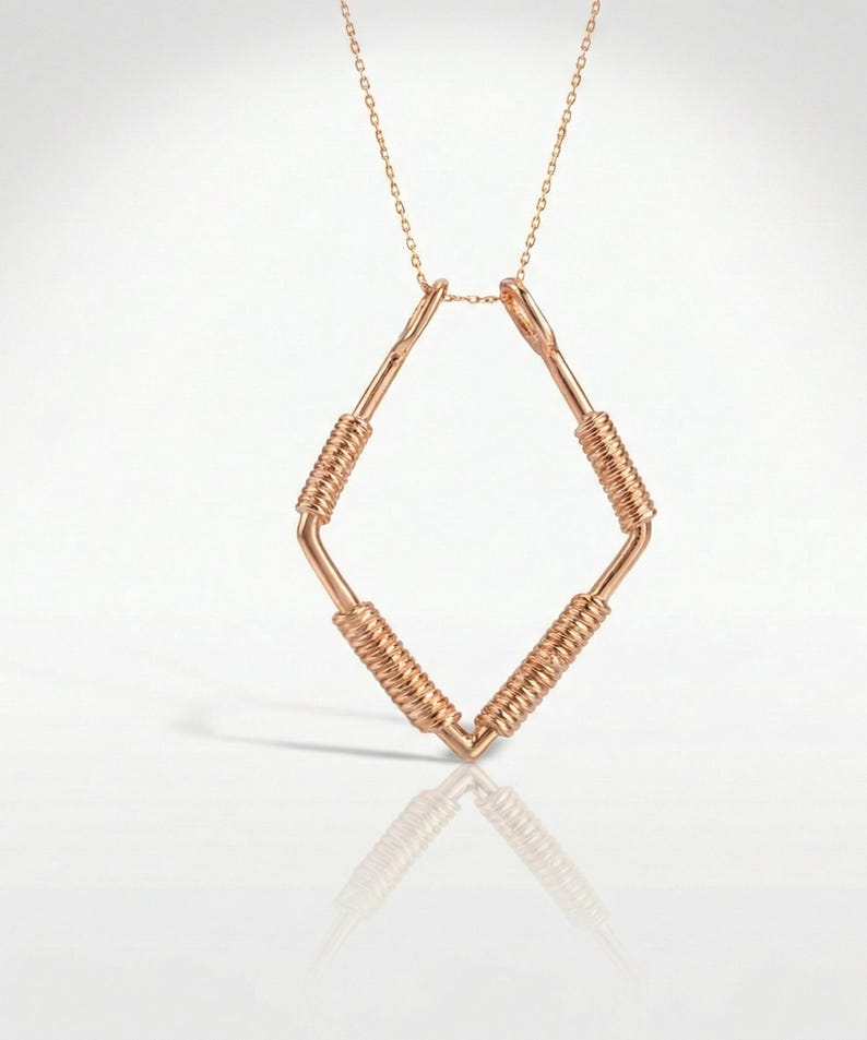 May include: Rose gold necklace featuring a geometric diamond-shaped pendant. The pendant has a wire-wrapped design on the diagonal bars, and is suspended from a delicate chain. The necklace is displayed on a white surface.