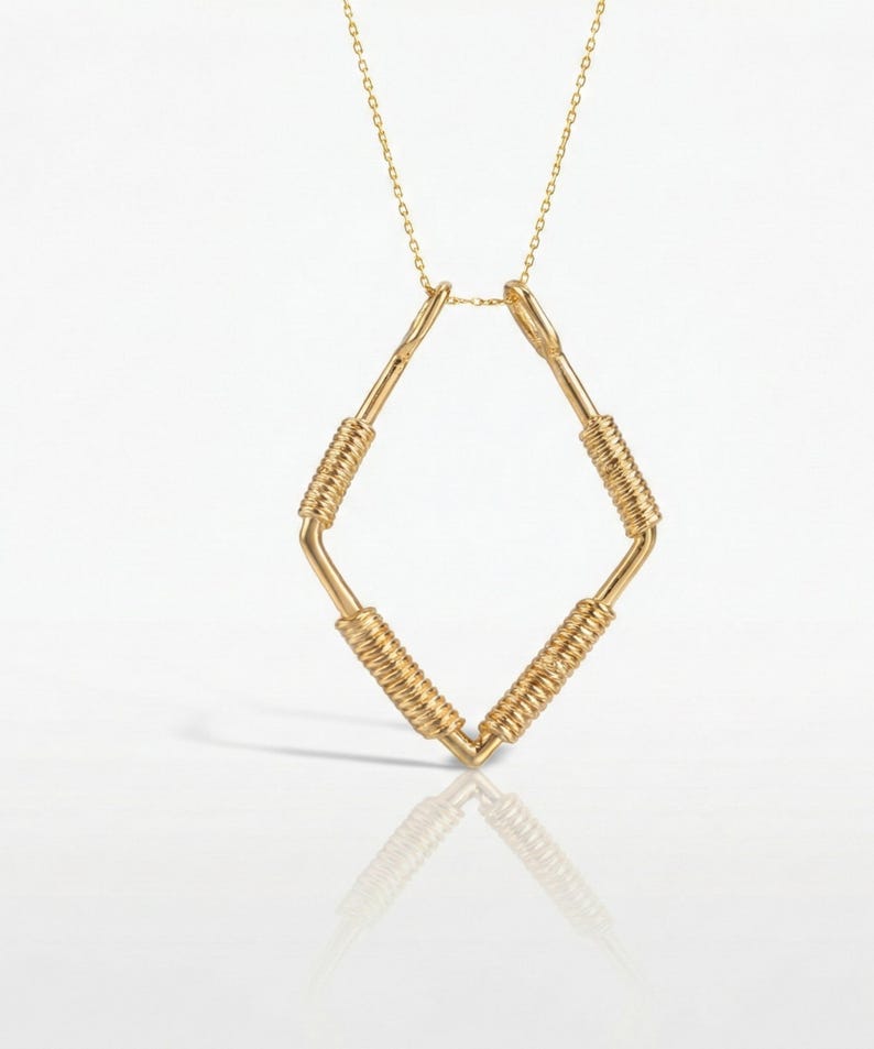 May include: A gold-colored necklace with a diamond-shaped pendant. The pendant is made of straight bars with coiled wire wrapped around the center of each bar. The necklace chain is delicate and gold-colored.