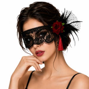Op de afbeelding: Een zwart kanten oogmasker met een donkerrode stoffen roos, een bijpassend rood kwastje, zwarte veren en wit tule met stippen. Het masker bedekt het ooggebied met ingewikkelde bloemmotieven en geschulpte randen langs de onderkant.