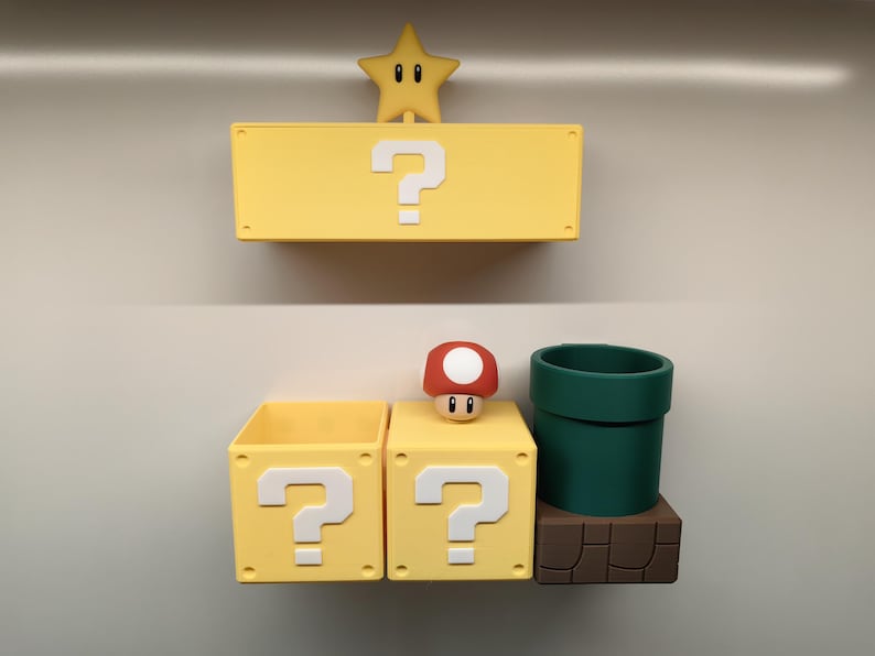 May include: A yellow question mark box, a star, a mushroom, and a green pipe, all inspired by a video game. The star is yellow with a smiling face. The mushroom has a red cap with white spots. The pipe is dark green.