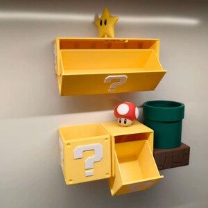 May include: Yellow storage boxes with question mark symbols, a green pipe, a red and white mushroom, and a yellow star. The boxes are mounted on a wall, creating a playful, themed display.