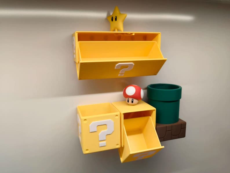 May include: Yellow storage boxes with question mark symbols, a green pipe, a red and white mushroom, and a yellow star. The boxes are mounted on a wall, creating a playful, themed display.