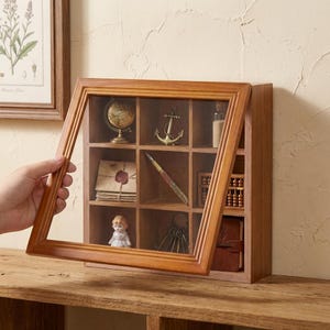 以下が含まれることがあります： ガラス張りの木製ディスプレイケース。ミニチュアのヴィンテージアイテムを展示しています。ケースには地球儀、錨、ペン、人形、その他の装飾品が入っています。ケースは明るい茶色の木材で作られています。