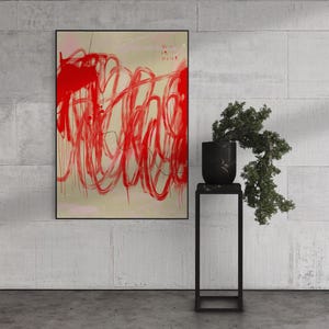 May include: A framed rectangular wall art piece featuring bold, gestural red paint strokes on a light beige background. The artwork includes small, faint text in the upper right corner. Beside the art is a black marble planter with a green plant.