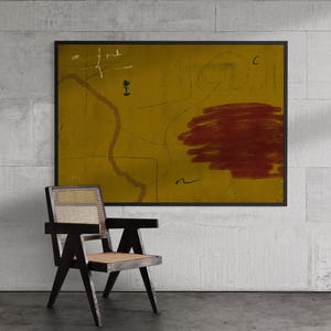 Puede incluir: Una pintura abstracta con un fondo amarillo mostaza y una gran forma roja texturizada. La obra de arte está enmarcada en negro y cuelga sobre una silla de madera negra con asiento y respaldo tejido.