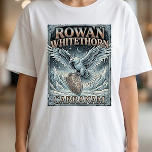 Puede incluir: Camiseta blanca con un gráfico detallado. El diseño presenta el texto "ROWAN WHITETHORN CARRANAM", un águila con las alas extendidas, un escudo y un paisaje montañoso en azul, gris y marrón.