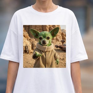 K&ouml;nnte beinhalten: Wei&szlig;es T-Shirt mit einem quadratischen Aufdruck. Der Aufdruck zeigt einen gr&uuml;nen Chihuahua in einem braunen Mantel und beigem Kragen vor einer W&uuml;stenkulisse. Der Hund streckt eine Hand aus. Ein Raumschiff ist im Hintergrund zu sehen.