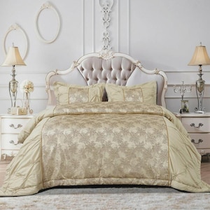 May include: A beige and gold floral patterned duvet cover set on a bed with a buttoned headboard. The set includes matching pillowcases. Two bedside tables with lamps and decorative items flank the bed.