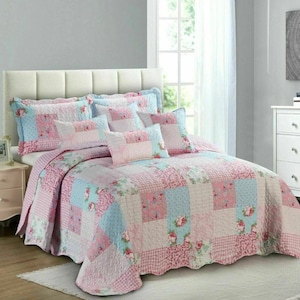 May include: A bed dressed with a patchwork quilt and matching pillows in pink and blue hues. The quilt has a scalloped edge and floral patterns. The bedding set includes a variety of textures and patterns, creating a cosy and inviting look.