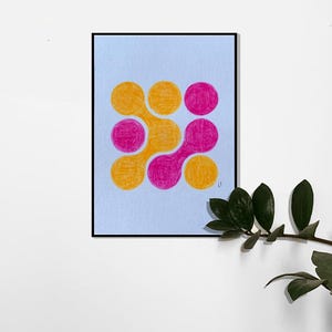 May include: An abstract artwork featuring a pattern of interconnected circles in shades of orange and pink. The design is set against a light blue background, framed in black, and presented on a white wall with a green plant in the corner.