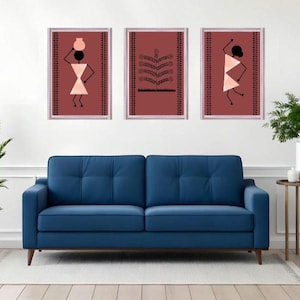May include: Three framed wall art pieces with abstract figures in a minimalist style. The artwork features figures in black and peach against a maroon background. A blue sofa and plants complete the room.