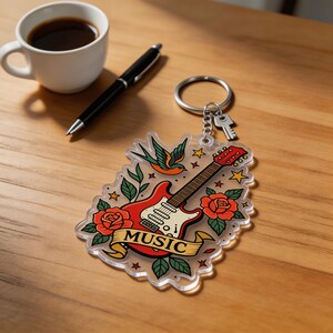 May include: A clear acrylic keychain featuring a red electric guitar, roses, a swallow, and the word "MUSIC" on a banner. The keychain is attached to a silver keyring with a key. The design has a tattoo-inspired aesthetic.