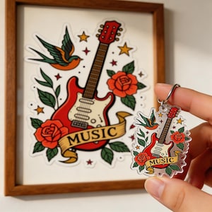 May include: A framed print and a keychain featuring a red electric guitar, roses, a swallow, and the word "MUSIC" on a banner. The guitar has a cream-colored body and a brown neck. The keychain is held by a person.