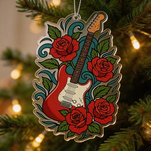 Op de afbeelding: Een gitaarvormige kerstversiering met een rode body, bruine hals en witte slagplaat. Versierd met rode rozen, groene bladeren en turquoise krullen. Opgehangen aan een zilveren draad, ideaal voor feestelijke decoraties.