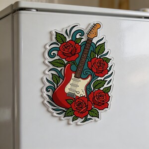 Op de afbeelding: Een rode elektrische gitaarsticker met een witte slagplaat, omringd door rode rozen en groene bladeren. Het ontwerp bevat turquoise krullen en is geplaatst tegen een transparante achtergrond.