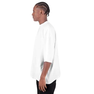 May include: A white, short-sleeved t-shirt with a mock neck. The shirt has a loose, oversized fit. The person in the image is wearing black pants. The background is plain white.