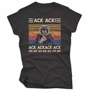 May include: Black t-shirt featuring a retro design with a creature illustration and the text "ACK ACK!". The design includes horizontal stripes in yellow, orange, red, and blue. The shirt is made of a soft material.